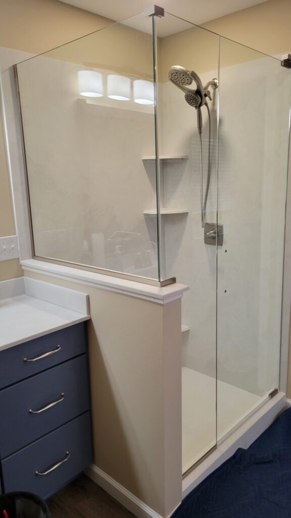 A clear glass walk-in shower with visible showerhead and shelves before applying privacy frost.